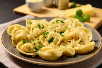 Plate of boiled dumplings with cheese and basil on black background