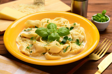 Bowl of boiled dumplings with sauce and basil on wooden background