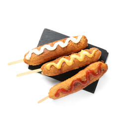 Black board of tasty corn dogs with different sauces on white background