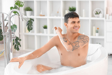 Handsome young man massaging his back in bathtub at home