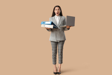 Shocked businesswoman with folder and laptop on beige background