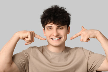Smiling young man with dental braces on light background