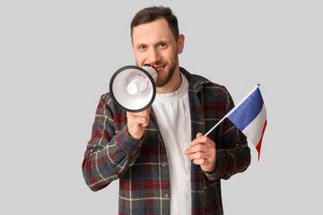 Young man with flag of France and megaphone on light background