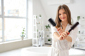 Beautiful young woman with round hair brushes in bathroom