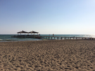 Fototapeta premium A wide pier on the beach leads to two gazebos or bungalows in the sea