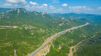 An impressive aerial view capturing the toll booth(Naplatna postaja) on the A6 Rijeka - Zagreb Motorway and the stunning peak of Kamenjak vrh. The motorway, known for its engineering marvels