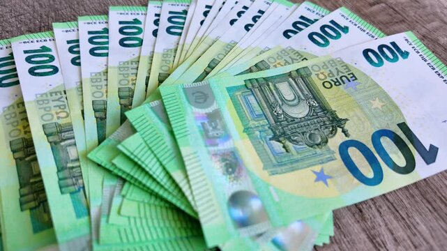 Person counts out 100 euro banknotes and places them one by one on a office desk