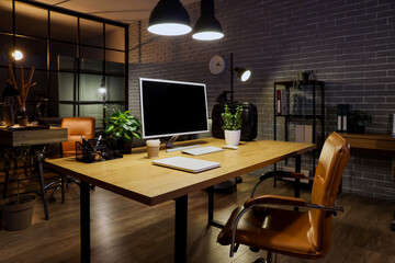 Workplace with blank computer, plants and glowing lamps in dark office