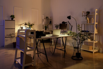 Interior of dark office with desks, plants and glowing lamps
