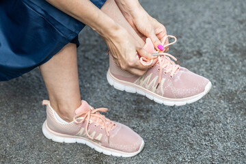 woman tying laces on sneakers while sitting on a bench. man tying shoelaces in the park. tying shoelaces with a bow. woman in skirt and sneakers. 