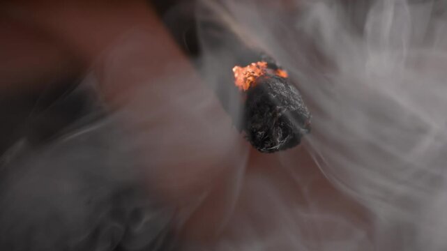 Close-up shot of a burning marijuana joint and blowing smoke