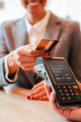 Vertical. Unrecognizable woman paying the bill with a contactless credit card in a restaurant. Close up image of a female holding a creditcard and giving a payment transaction to the cashier dataphone