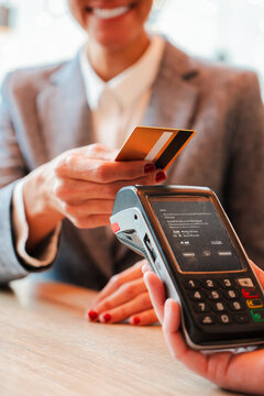 Vertical. Unrecognizable woman paying the bill with a contactless credit card in a restaurant. Close up image of a female holding a creditcard and giving a payment transaction to the cashier dataphone