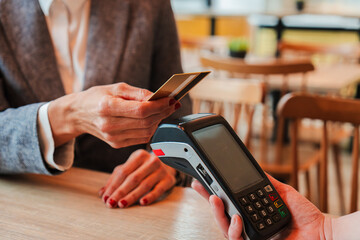 Unrecognizable woman paying the bill with a contactless credit card in a restaurant. Close up image of a female holding a creditcard and giving a payment transaction to the cashier dataphone.