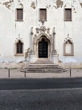 Front view of the historic, weathered facade and decorative Manueline portal of the Igreja Paroquial de Sao Bartolomeu do Beato in Lisbon, Portugal.