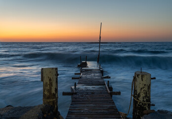 Obraz premium Old wooden bridge into the sea with a beautiful sunset