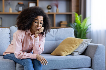 Obraz premium Woman looking sad and reflective sitting on couch in modern living room showing emotions and contemplation