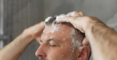 Closeup shot of man washing hair with shampoo, taking shower with eyes closed in bathroom. Male haircare and bodycare concept