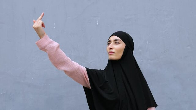 Muslim woman in hijab shows protest gesture middle finger. Gesture expresses strong emotions and disagreement. Traditional image and provocative gesture attracts attention, challenging stereotypes.