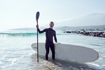 senior man comes out of the water holding a paddle board wearing surf suit