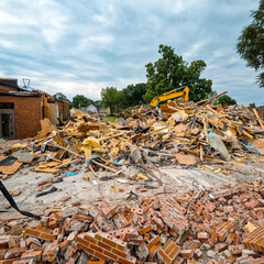Fototapeta premium A large brick building has just been demolished. A pile of red bricks, wood insulation and debris are stacked in a pile. Bulldozer in background of view. Large demolition construction site.