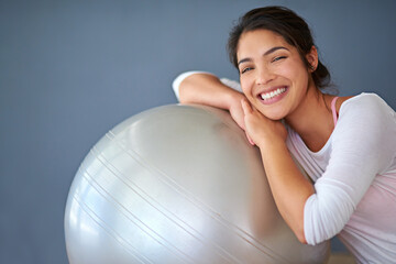 Fototapeta premium Health, happy woman and yoga ball in portrait on floor for core workout, balance and weight loss in studio. Yogi, smile and training equipment for fitness, wellness and cardio on grey background