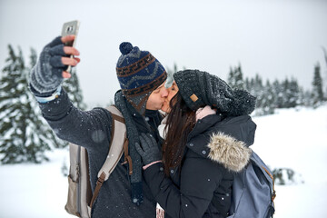 Winter, snow and couple with kiss for selfie, document memories and profile picture for social media. Married people, man and woman for photography in vacation, bonding and anniversary in Canada