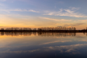 a row of trees without foliage and a lake shore at sunset in spring