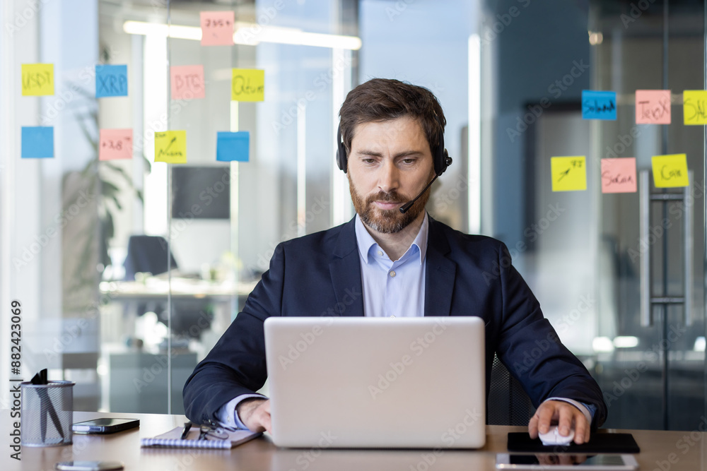 Wall mural serious and focused man with headset phone works inside office with laptop, businessman in business 