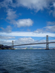Obraz premium Scenic view of San Francisco-Oakland Bay Bridge and Oakland with container terminal in the background, California, USA seen from the water against blue sky with clouds