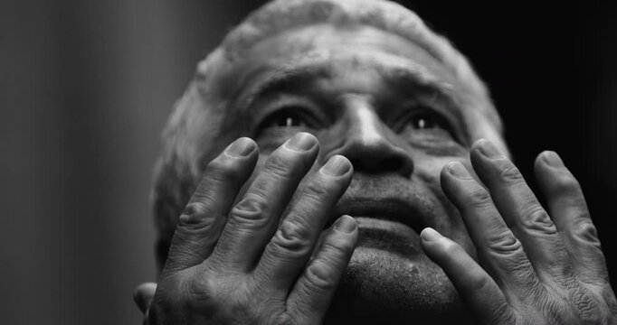 Speechless Senior man feeling the presence of God looking upwards raising hands in spiritual contemplation feeling tearful and in awe to a powerful divine illumination in intense black and white