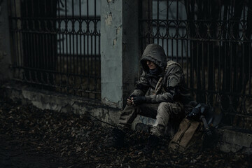 A man in a gas mask and camouflage sits on the ruins with a flower in his dirty hands. The concept...