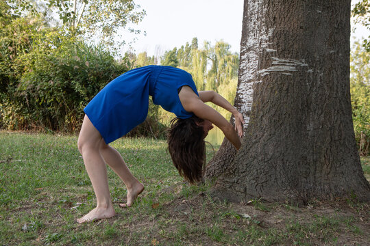 Young woman performing backbend yoga pose by tree in park