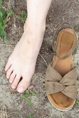 Woman choosing between putting sandals or walking barefoot on dirty ground