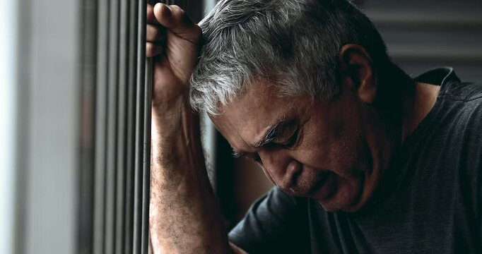 Sad depressed elderly man crying in despair gripping metal bar looking down with tearful close-up face in deep melancholy and regret. Sorrow older person