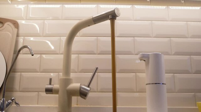 Dirty rusty water flowing from the home kitchen tap after the human hand turns on the faucet. Contamination water problem. Faucet water pollution. 4K