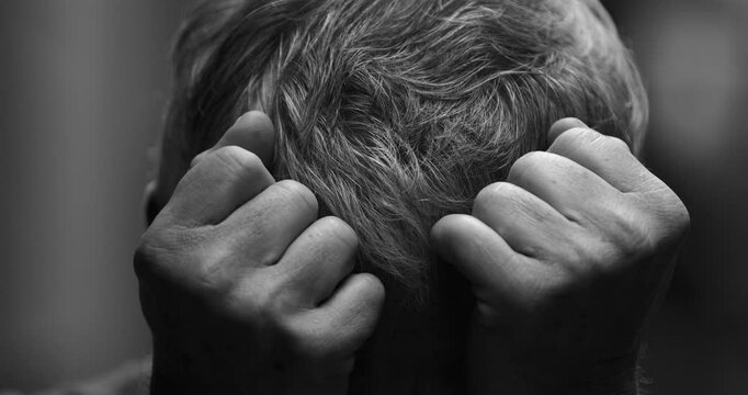 Depressed senior man in distress covering face with hands looking down in emotional pain, gray hair older 70s person in deep sorrow in intense dramatic black and white