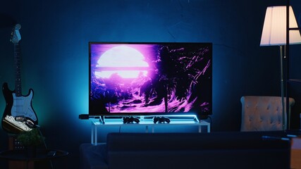 Zoom in shot on TV screen showing 3D render animations in empty stylish neon lit home studio interior. Modern apartment illuminated with RGB lights at night and artwork decorating the walls