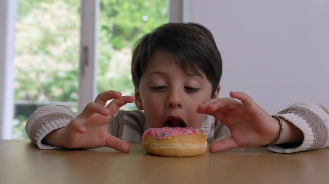 Young boy leaning over a table, eagerly eyeing a colorful sprinkled donut, showcasing the temptation and excitement of delayed gratification as he reaches towards it