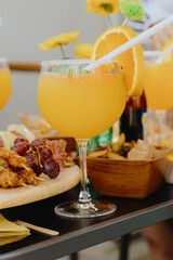 Glass of orange cocktail with snacks on the table.