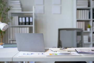 Laptop computer is sitting open on a desk in a quiet office, surrounded by reports and office...