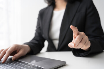 Confident businesswoman in black suit typing on laptop, pointing at you. Exudes power, authority,...