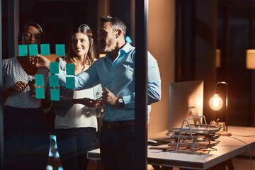 Night, writing and business people with glass board for sticky note, project ideas or brainstorming...