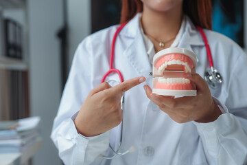 Female doctor in white lab coat explains dental hygiene with denture model in clinic, emphasizing oral health. Professional, knowledgeable, promoting healthy smiles