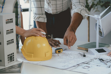 Three architects are discussing a project with a model of a wind turbine and a model of a building,...