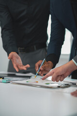 Fototapeta premium Business people wearing suits having a meeting in an office setting, discussing and pointing at financial charts displayed on a table