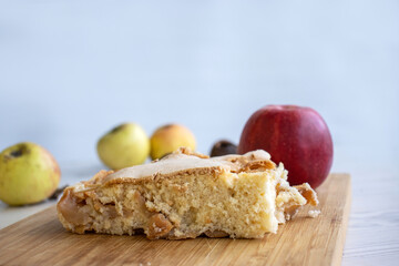 Piece of traditional thanksgiving apple cinnamon pie, apples and walnuts on the wooden cutting board on the white table. Homemade baked fruit tart with golden crust. Close up, copy space, top view.