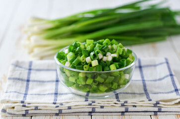 Chopped scallions or young spring onion in a clear glass bowl, on a kitchen table.