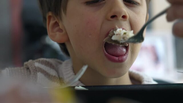 Close-up of a young boy reluctantly eating rice from a fork, highlighting the challenges of mealtime with children, showcasing a moment of parental care and persistence during feeding