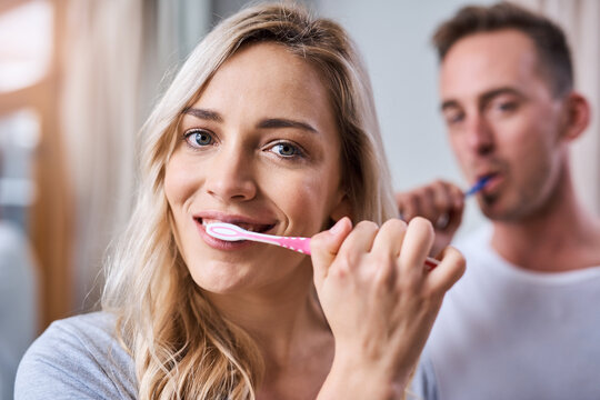 Portrait, dental and happy woman brushing teeth with man in bathroom for oral hygiene, fresh breath or morning routine. Home, wellness and couple with toothbrush for whitening, cleaning or mouth care